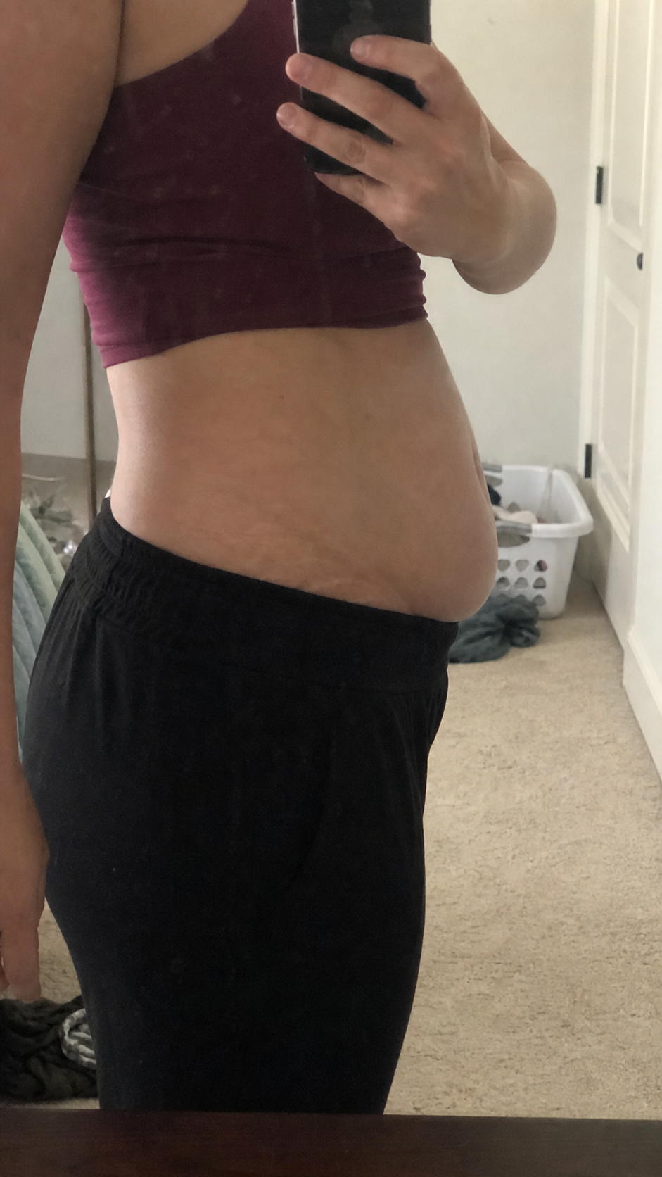 Raw side-profile phone mirror image of an adult postpartum midsection