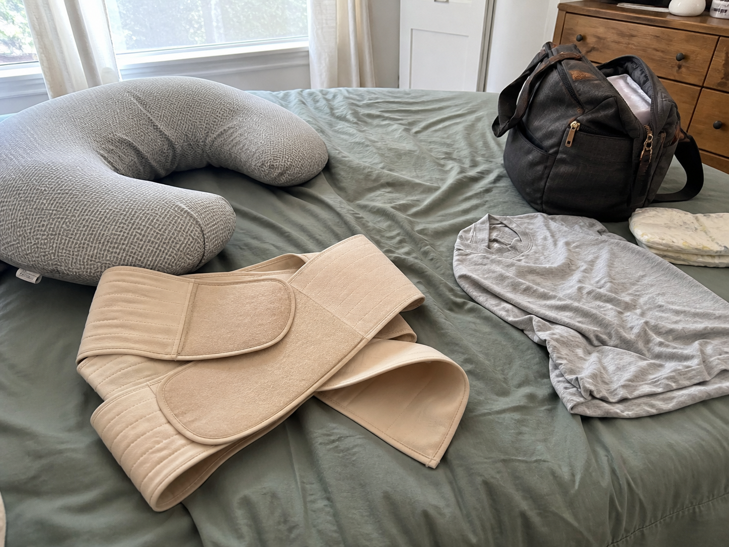A bulky generic postpartum wrap left on a bed beside everyday baby items