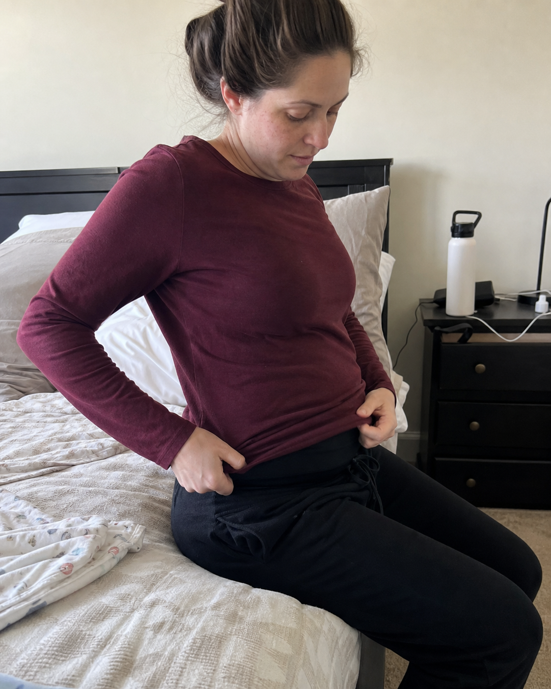 A seated postpartum mother adjusting a bulky band beneath her shirt